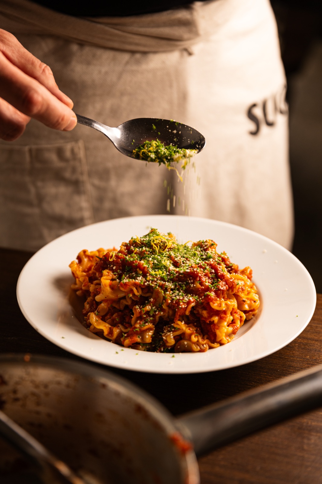 Ragù de mafaldine parsemé de gremolata, devant un tablier SUGO