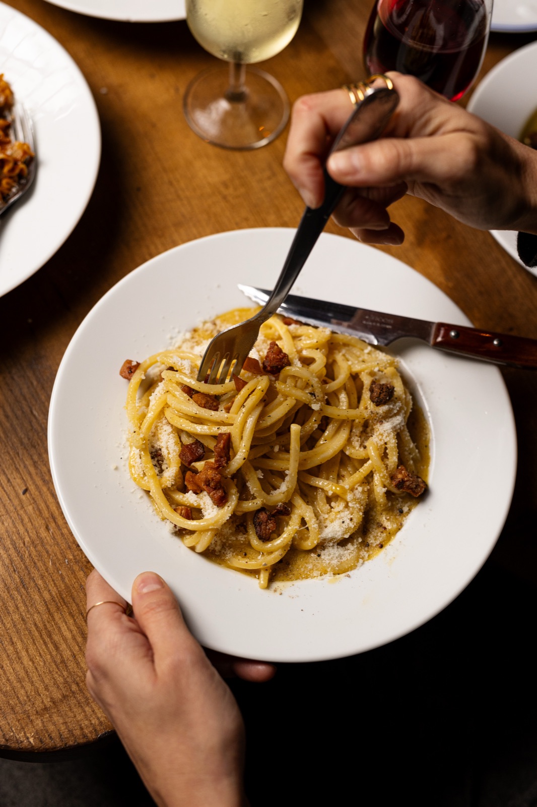 Assiette de carbonara, fourchette plantée dans les spaghetti, sur une table en bois